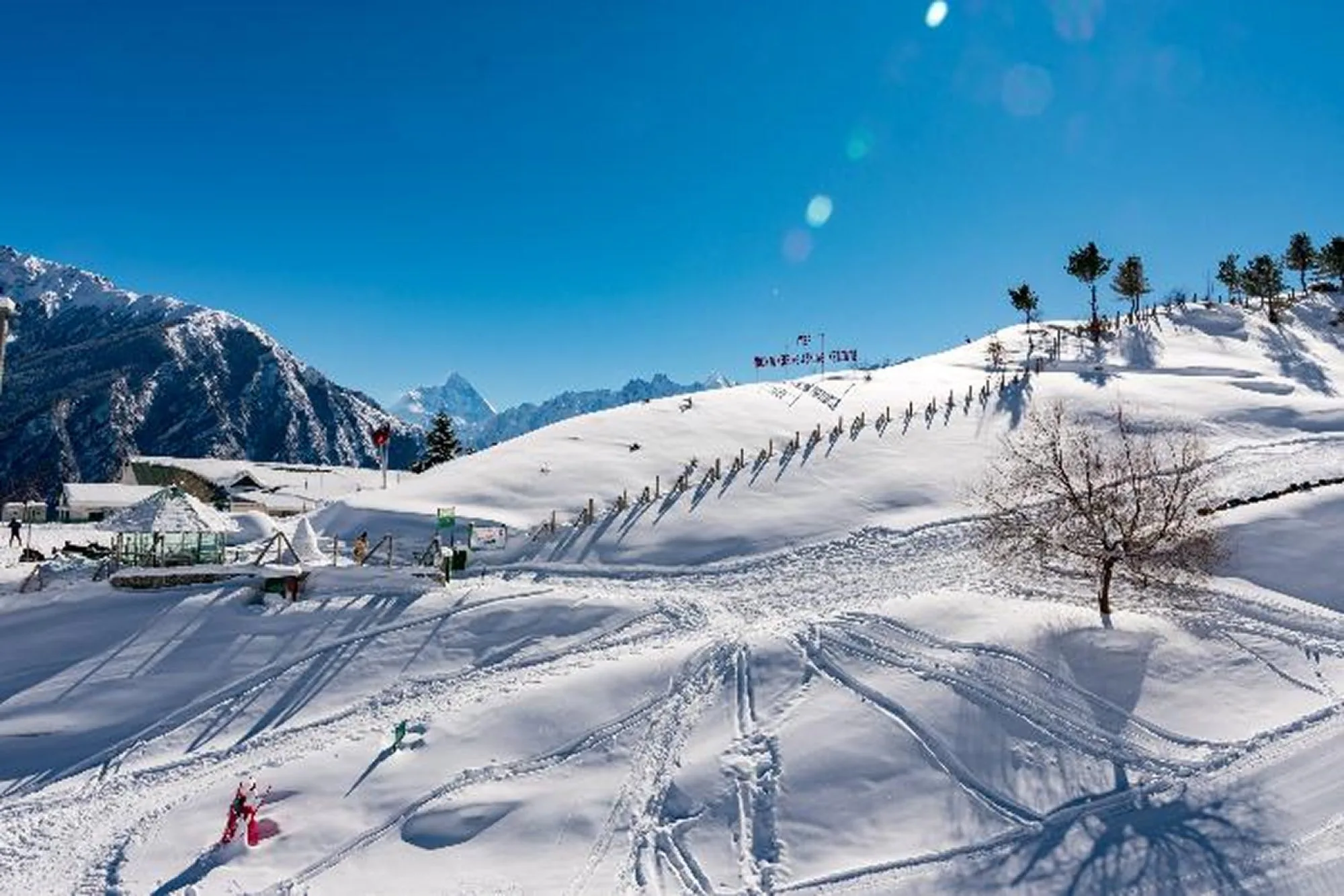 Ski tracks cut across deep snow, with slalom poles running up the ridge and peaks on the horizon