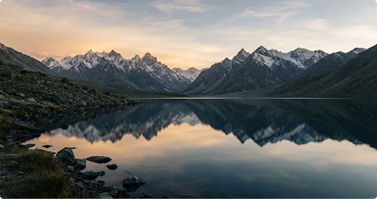 Snow peaks mirrored in a still high-altitude lake at sunset