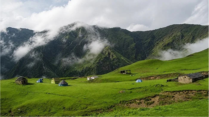 Tents pitched on a rolling green meadow with cloud spilling over the ridge behind
