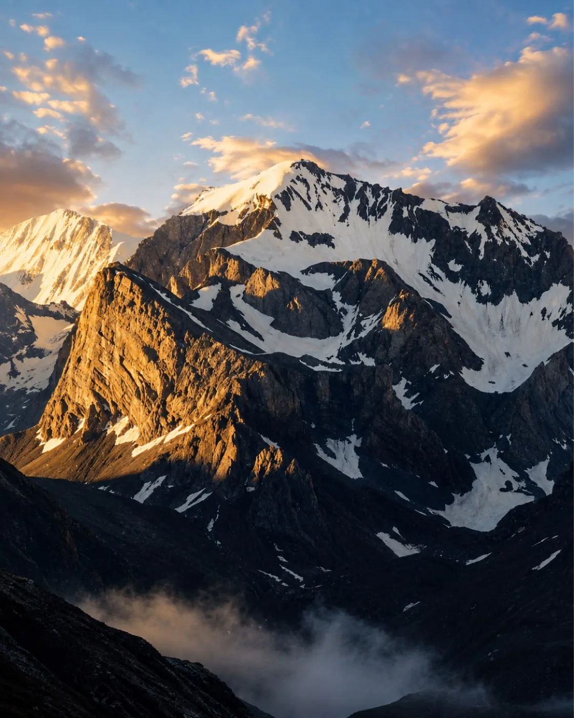 A snow peak lit gold at sunrise, with cloud lying in the valley below the ridge
