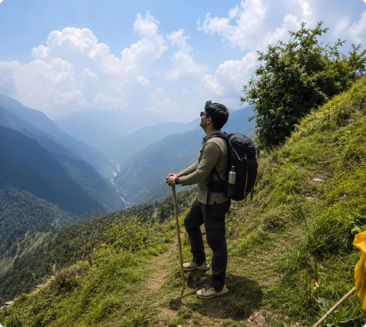 A trekker pausing on a green ridge to look out over a Himalayan valley