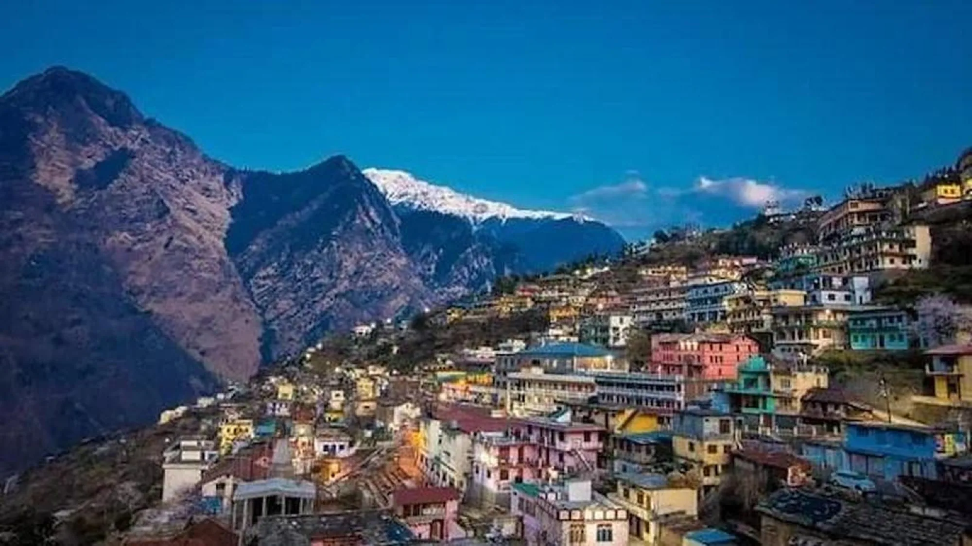 Brightly painted houses stacked up a hillside at dusk, below a steep mountain wall