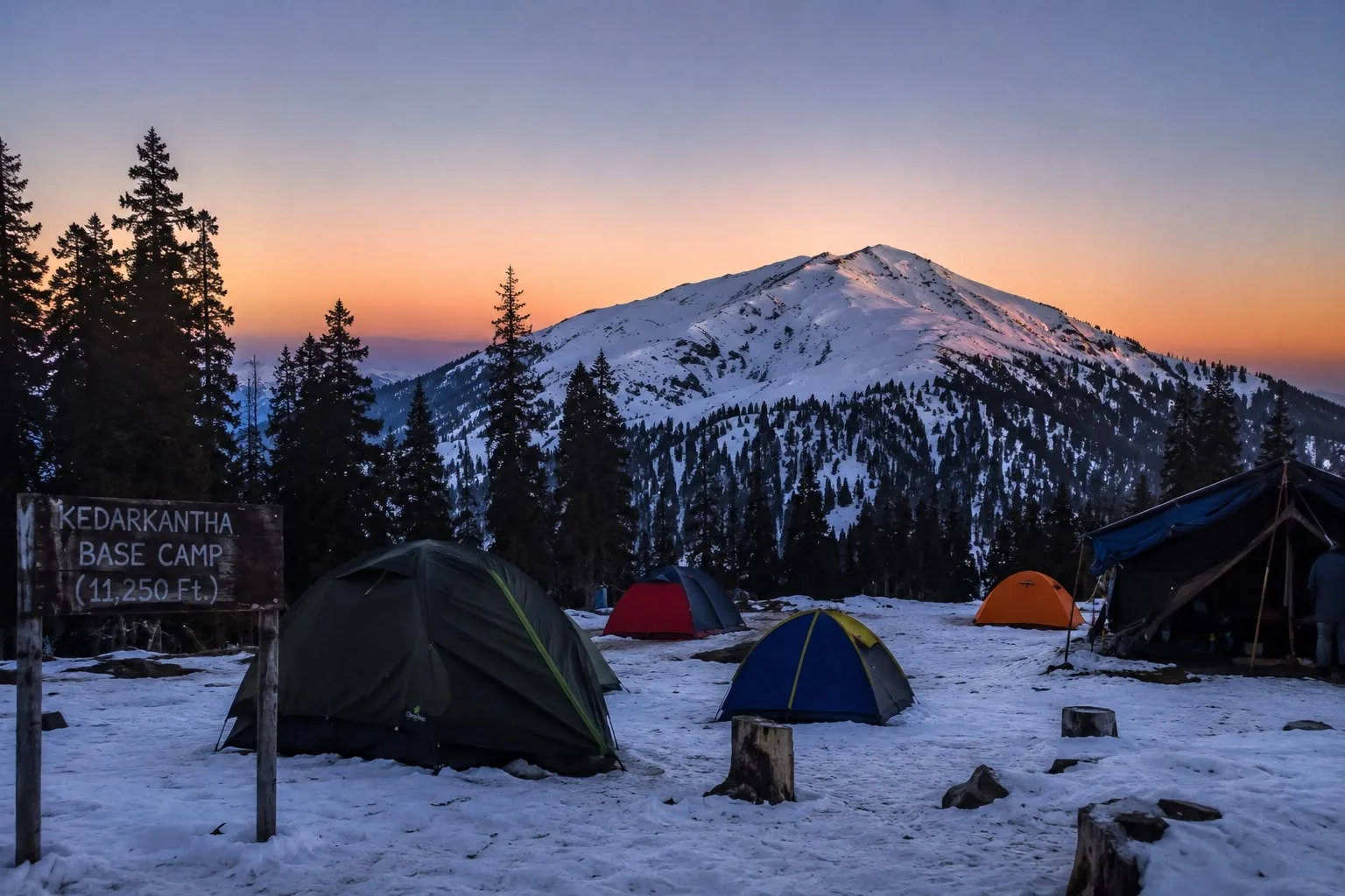 Dome tents pitched on packed snow at dusk below a conical snow-covered summit, a wooden sign in the foreground reading "Kedarkantha Base Camp, 11,250 ft"
