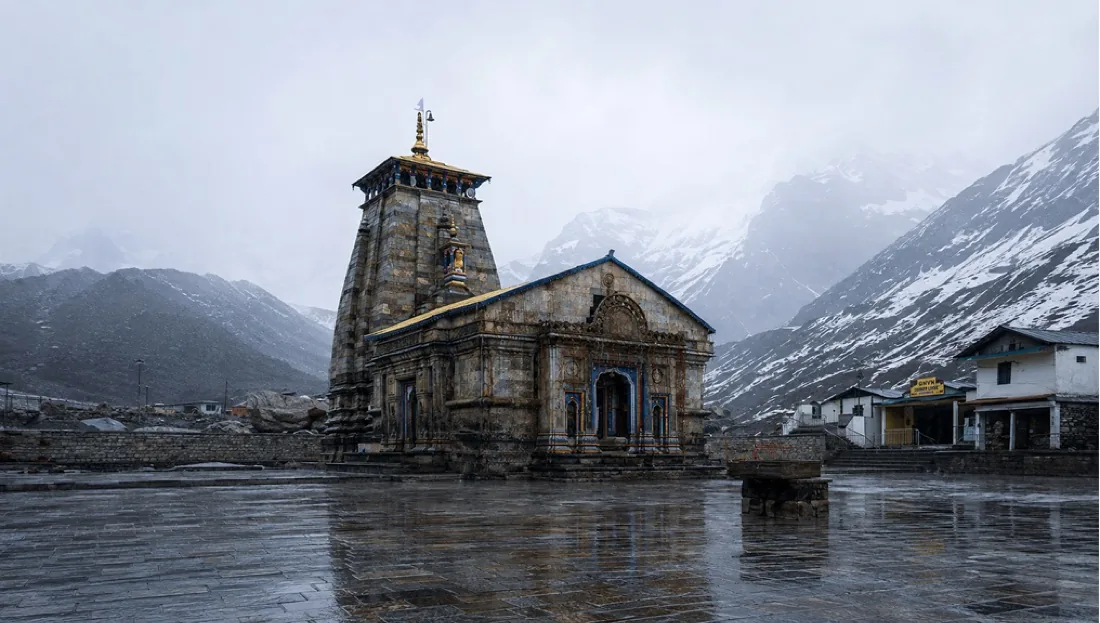The grey stone Kedarnath temple on its wet flagstone plaza below snow-streaked peaks