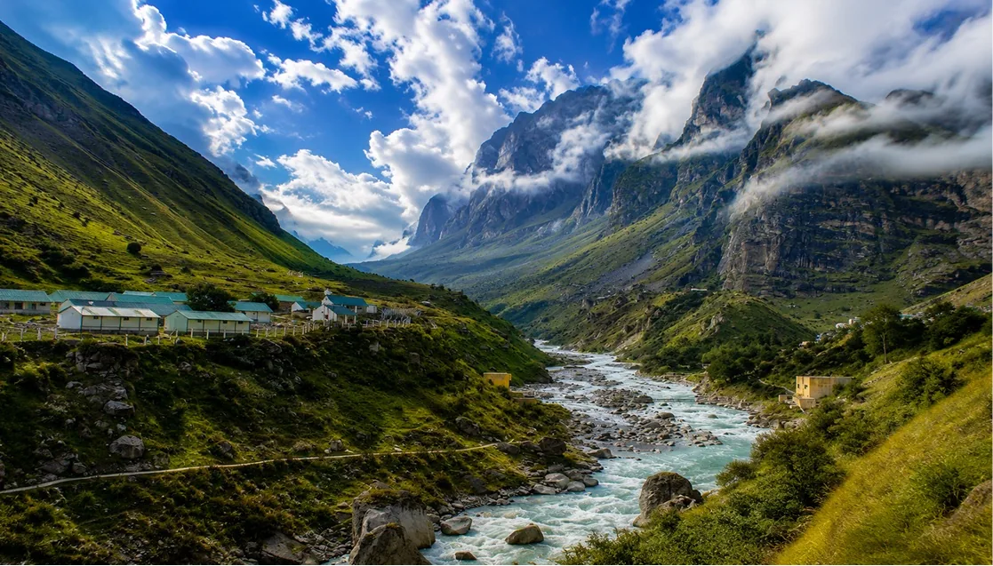 A glacial river running through a steep green valley below cloud-wrapped cliffs