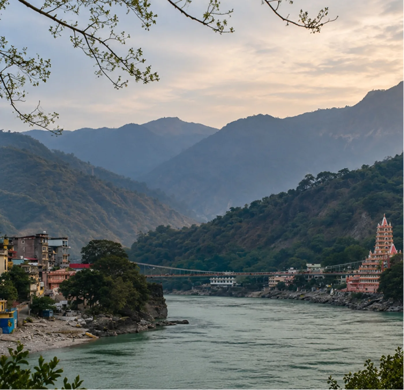 A river curving past a suspension bridge and a riverside temple at dusk