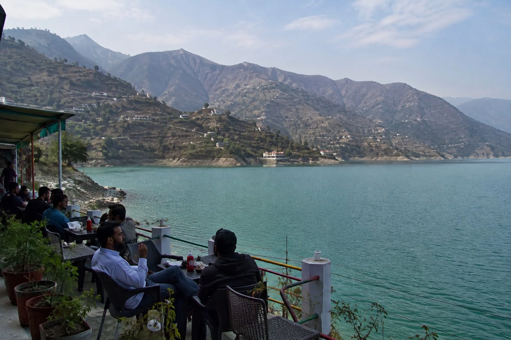 Tables on a cafe terrace at the edge of the water, below dry terraced slopes